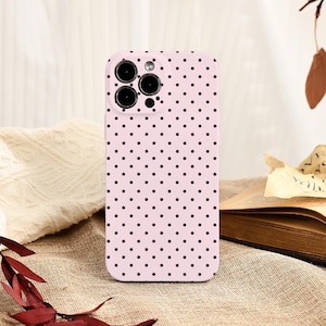 May include: A pink phone case with a repeating pattern of small black polka dots. The case has cutouts for the phone's camera and buttons. The phone case is a solid color and has a smooth texture.