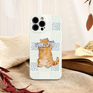 May include: A white phone case featuring a cartoon orange tabby cat holding two fish. The case has a floral pattern with blue flowers and a grid design. The phone's camera lenses are visible at the top.