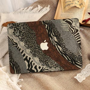 Puede incluir: Funda para portátil con un diseño de estampado animal único. El diseño presenta patrones marrones, grises y negros, con rayas de leopardo y cebra. Se ve un logotipo de Apple blanco. La funda está sobre una superficie de tono neutro.
