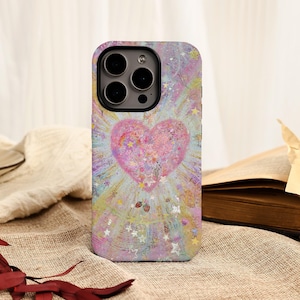 May include: A phone case featuring a pink heart design with a rainbow and star accents. The case has a colorful, pastel background with a textured appearance. The phone case is on a neutral-colored surface.