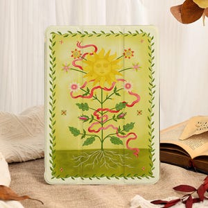 May include: A rectangular tablet case featuring a light yellow background with a central illustration of a yellow sun with a face above a green plant with roots. The design includes pink ribbons, small flowers, and a green leaf border frame.