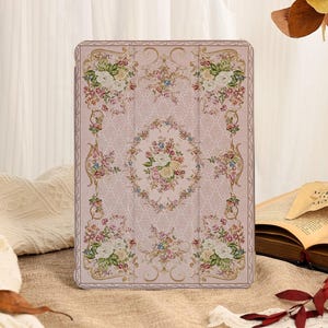 May include: A rectangular tablet case featuring a light pink background with a repeating damask pattern and a central oval medallion filled with colorful floral bouquets of roses and greenery, framed by ornate gold-toned scrollwork borders.