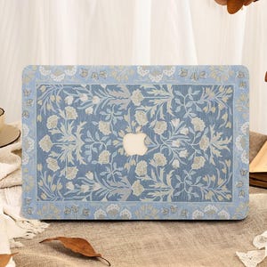 Puede incluir: Una funda azul para portátil con un estampado floral. La funda presenta un fondo azul claro con un diseño repetido de flores y hojas blancas y beige. El logotipo de Apple es visible en el centro.