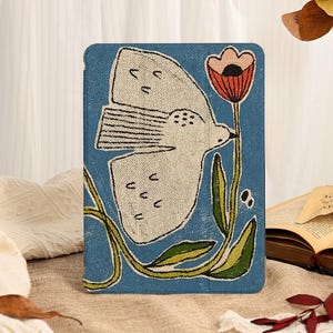 May include: A rectangular tablet case featuring a blue background with a white bird in flight, a single orange and black flower on a green stem, and green leaves. The design has a textured, printed appearance on the front surface of the case.