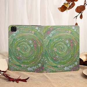 Może przedstawiać: Zielone etui na tablet z kwiatowym wzorem. Etui ma spiralny wz&oacute;r z białymi i r&oacute;żowymi kwiatami na zielonym tle. Etui ma chronić tablet.