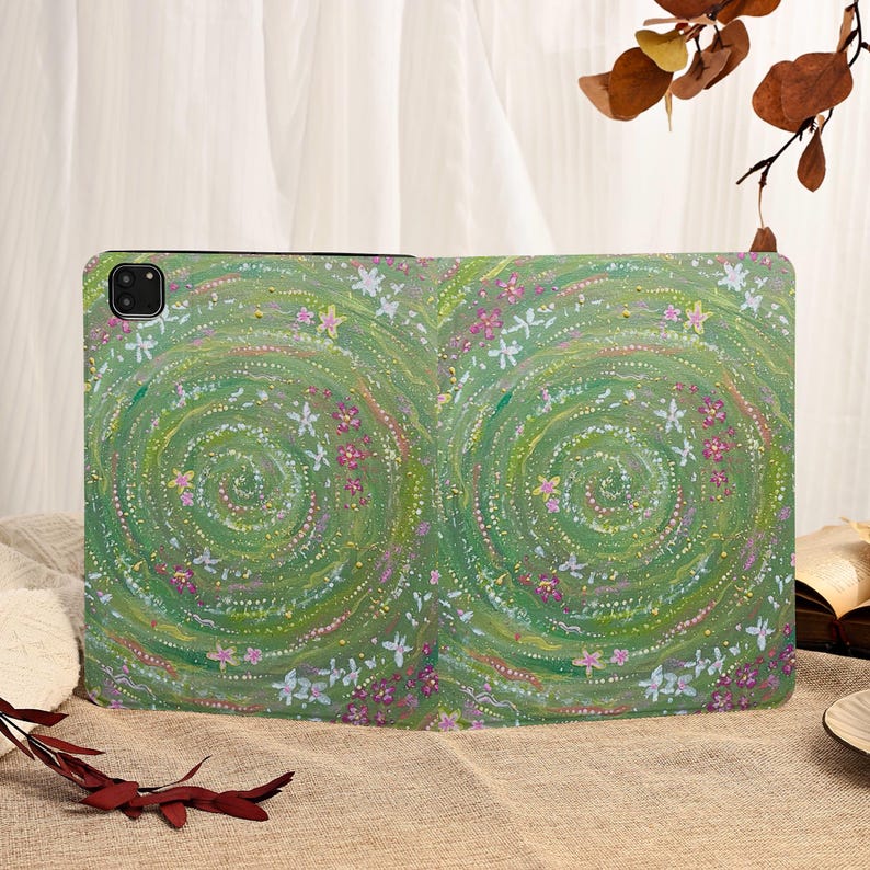 Może przedstawiać: Zielone etui na tablet z kwiatowym wzorem. Etui ma spiralny wz&oacute;r z białymi i r&oacute;żowymi kwiatami na zielonym tle. Etui ma chronić tablet.