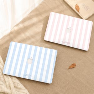 May include: Two laptop cases featuring vertical stripes. One case has light blue and white stripes with the name DAISY printed in a serif font. The other case has light pink and white stripes with the name JOANNA printed in a serif font. Both cases feature a central cutout for an Apple logo.