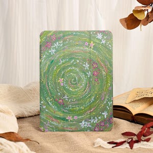 Może przedstawiać: Zielone etui na tablet z kwiatowym wzorem. Etui ma spiralny wz&oacute;r z białych, r&oacute;żowych i ż&oacute;łtych kwiat&oacute;w na zielonym tle. Prostokątne etui wydaje się być wykonane z wytrzymałego materiału.