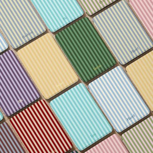 Könnte beinhalten: Eine Auswahl rechteckiger Untersetzer mit vertikalen Streifen in verschiedenen Farben, darunter Blau, Grün, Gelb und Rot. Einige Untersetzer tragen aufgedruckte Namen wie "Hudson" und "Lucas".