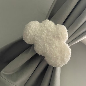 May include: White fluffy cloud-shaped curtain tieback. The tieback is made of a soft, plush material and is perfect for adding a touch of whimsy to any room.