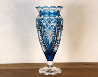 May include: A tall, blue glass vase with intricate cut glass designs. The vase has a wide base and a narrow neck.