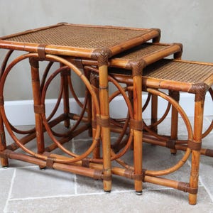 Puede incluir: Juego de tres mesas nido hechas de bambú y ratán tejido. Las mesas tienen una parte superior cuadrada y patas redondeadas, con un acabado marrón natural. La mesa más grande mide aproximadamente 51 cm de ancho, 51 cm de profundidad y 51 cm de alto.