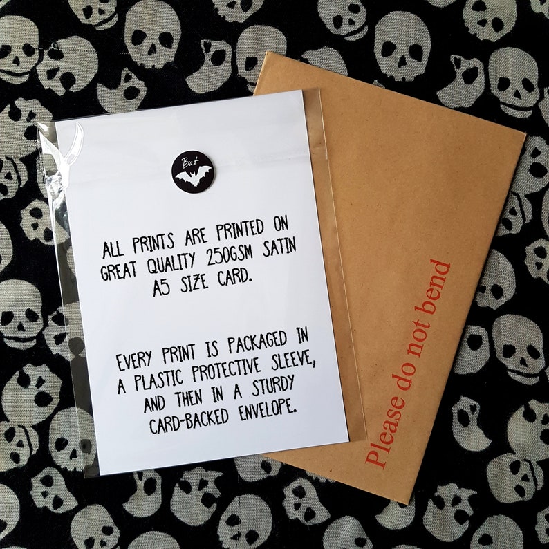 May include: A white card with black text that reads "All prints are printed on great quality 250gsm satin A5 size card. Every print is packaged in a plastic protective sleeve, and then in a sturdy card-backed envelope." The card is sitting on a black and white fabric with a skull pattern. A brown envelope with the text "Please do not bend" is partially visible in the upper right corner of the image.