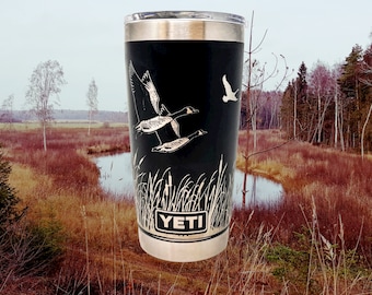 May include: A black Yeti tumbler with a white design of flying geese and reeds. The tumbler has the word "YETI" printed on the front.