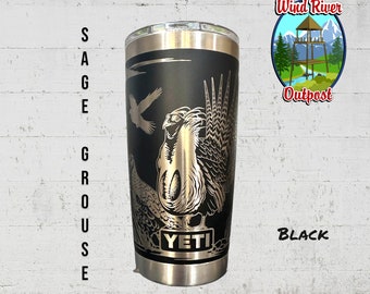 May include: A black Yeti tumbler with a gold metallic design of a sage grouse. The tumbler has the words "Wind River Outpost" and "YETI" on it. The text "BLACK" is also visible in the image.