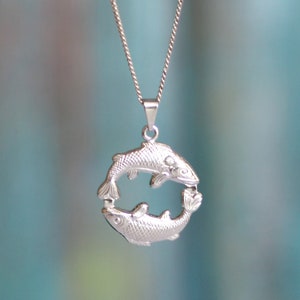 May include: A silver necklace with a pendant shaped like two fish intertwined in a circle.