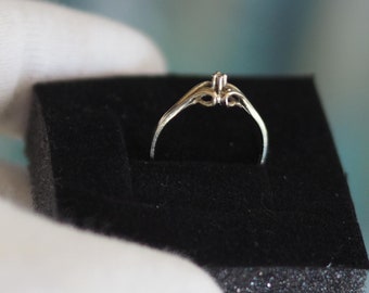 Puede incluir: Un anillo de plata con un pequeño diamante en el centro. El anillo está sentado en una caja de anillo de terciopelo negro.