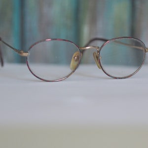 May include: A pair of gold-rimmed eyeglasses with red and black patterned frames.