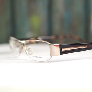 May include: Gold-tone metal eyeglasses with brown tortoise shell temples. The glasses have a rectangular shape and say "Made by Marc Jacobs" on the temple.