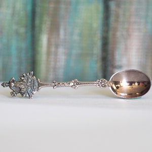 Puede incluir: Una cucharita de plata con un diseño ornamentado en el mango. La cuchara tiene un cuenco redondeado y un mango decorativo con un motivo floral.