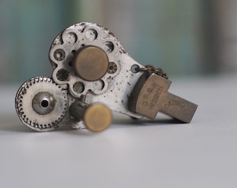 May include: A silver and brass mechanical pencil with a gear system and a cross-shaped charm with the text "D.F.G.M.  Reg.Des.Ges.  GERMANY".