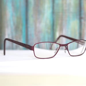 May include: A pair of burgundy-coloured eyeglasses with a rectangular frame and clear lenses.