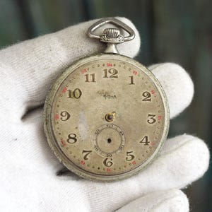 May include: Vintage pocket watch with a silver case and a cream-coloured face. The watch has black numerals, red markers, and a small seconds dial. It features a silver loop at the top.