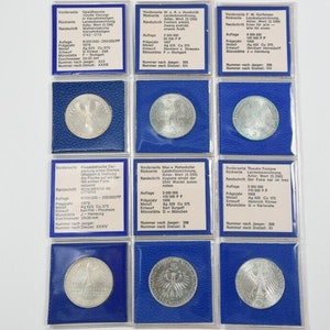 Può includere: Nove monete tedesche d'argento in contenitori di plastica blu con testo bianco che descrive le monete. Le monete presentano un design di aquila tedesca.