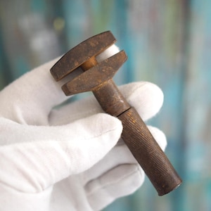 Puede incluir: Una llave inglesa antigua y oxidada con mango de madera. La llave está sostenida en una mano enguantada.