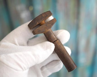 May include: A rusty, antique adjustable wrench with a wooden handle. The wrench is held in a gloved hand.