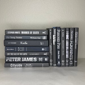 May include: A collection of hardcover books with dark gray covers. Titles include "Manner of Death," "Knife," and "Poisoned Pins." The spines display white text, and the books are stacked on a white surface.