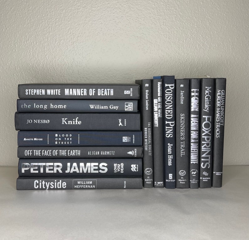 May include: A collection of hardcover books with dark gray covers. Titles include "Manner of Death," "Knife," and "Poisoned Pins." The spines display white text, and the books are stacked on a white surface.