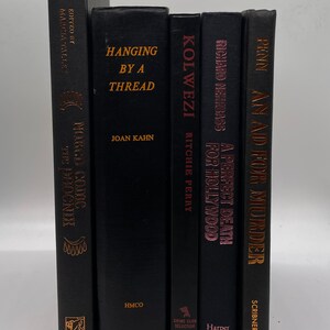 May include: A collection of six hardcover books with black covers and gold or pink lettering. Titles include "Hanging by a Thread" and "A Perfect Death for Hollywood". The books are arranged vertically.