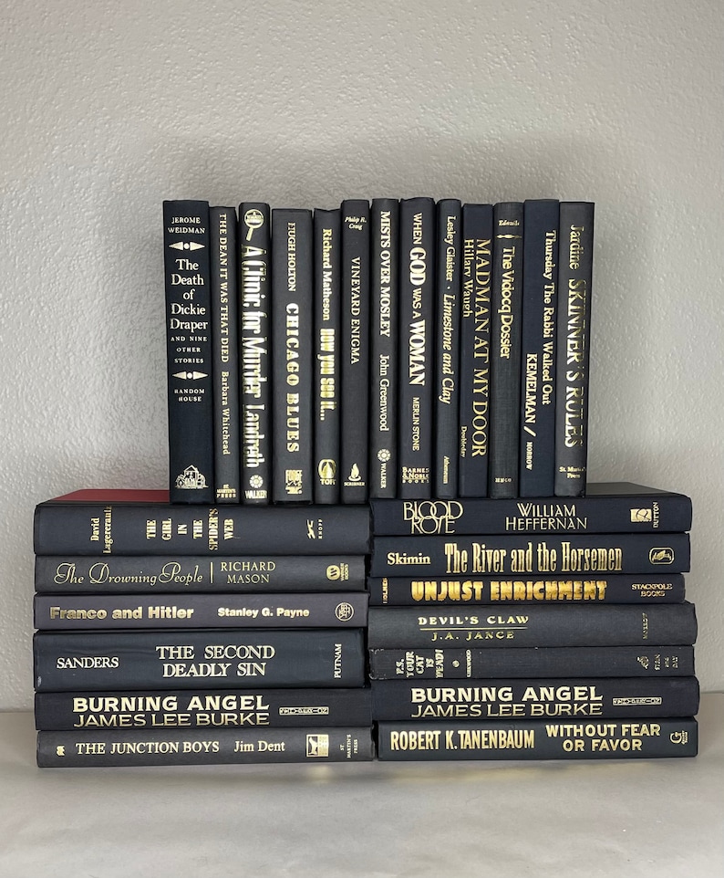 May include: A collection of hardcover books with black covers and gold lettering. The titles and authors are visible, including "Burning Angel" and "The Death of Dickie Draper." The books are stacked neatly, creating a visually appealing arrangement.