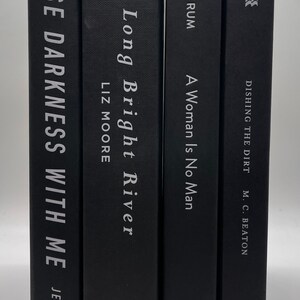 May include: Four hardcover books with black covers are displayed. The titles and authors are printed in white. The books include "Chase Darkness With Me" by Jensen, "Long Bright River" by Liz Moore, "A Woman Is No Man" by Etaf Rum, and "Dishing the Dirt" by M.C. Beaton.