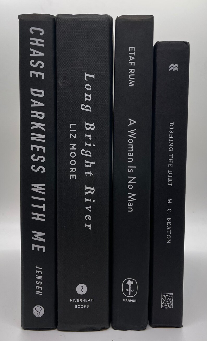 May include: Four hardcover books with black covers are displayed. The titles and authors are printed in white. The books include "Chase Darkness With Me" by Jensen, "Long Bright River" by Liz Moore, "A Woman Is No Man" by Etaf Rum, and "Dishing the Dirt" by M.C. Beaton.