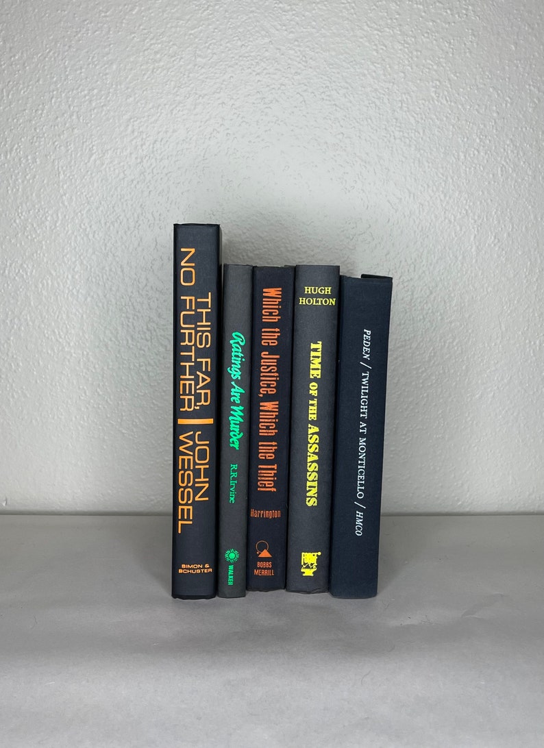 May include: A collection of hardcover books with dark covers and titles in gold and white. The titles include "This Far, No Further", "Ratings Are Murder", and "Time of the Assassins". The books are arranged vertically.