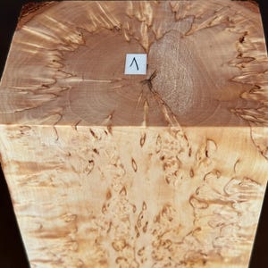 May include: A rectangular block of light-colored wood featuring a complex, swirling burl grain pattern throughout its surface. The top face displays a central growth ring pattern with a small white square label marked with the number 1.