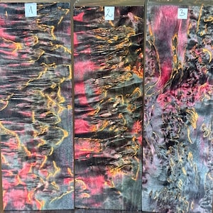 May include: Three rectangular wooden blocks featuring a vibrant burl grain pattern in shades of black, magenta, and gold. Each block is labeled with a white paper tag numbered one, two, or three, displaying intricate natural wood textures.