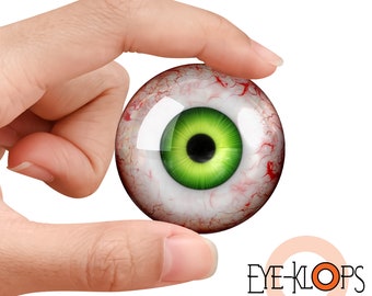 May include: A realistic-looking eyeball with a green iris and red blood vessels. The eyeball is being held between two fingers.