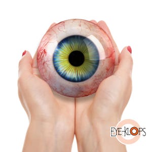 May include: A spherical glass eye prop featuring a realistic iris with a yellow center and blue outer ring, surrounded by a white sclera with detailed red blood vessels. The text EYE-KLOPS is printed in the bottom right corner of the image.