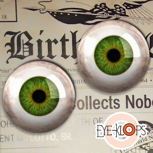 May include: Two realistic-looking green glass eyes with black pupils and a white sclera. The eyes are on a white background with text that reads "Birth" and "Collects Nob."