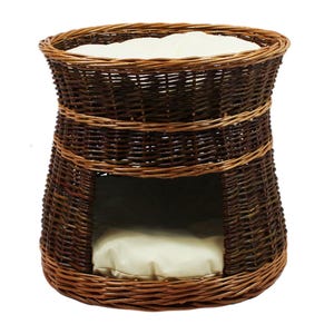 May include: A brown wicker cat bed with two cushioned areas. The bed has a round top and a lower opening with a cushion.