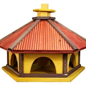 May include: A wooden bird feeder with a red and brown roof and yellow sides. The feeder has six feeding stations and is shaped like a hexagon.
