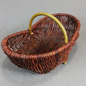 Peut inclure: Un panier en osier brun avec une poignée verte. Le panier est de forme ovale et présente un motif tissé.