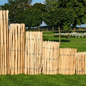Op de afbeelding: Vijf verschillende maten houten schuttingen, gemaakt van natuurlijke houten latten die met draad aan elkaar zijn geweven. De schuttingen zijn gestapeld op een gazon.