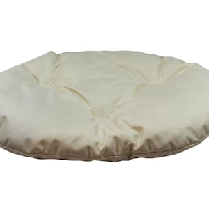 May include: A cream-colored round cushion with a tufted design. The cushion is made of a soft, plush fabric and has a slightly rounded shape.
