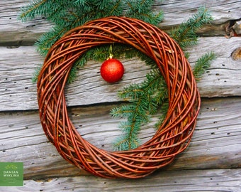 May include: A brown wicker wreath with a red Christmas ornament hanging on it. The wreath is hanging on a wooden wall.