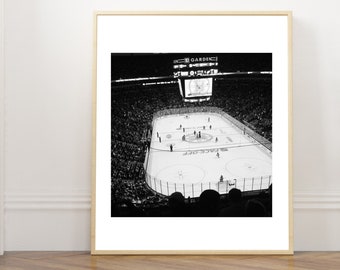 Puede incluir: Una impresión enmarcada en blanco y negro que muestra una vista elevada de un partido de hockey sobre hielo en el TD Garden. El estadio cuenta con un gran marcador central con información del juego, jugadores en el hielo y espectadores.