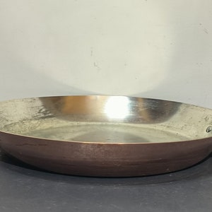 May include: A copper frying pan with a black handle. The pan has a shiny, slightly worn surface.